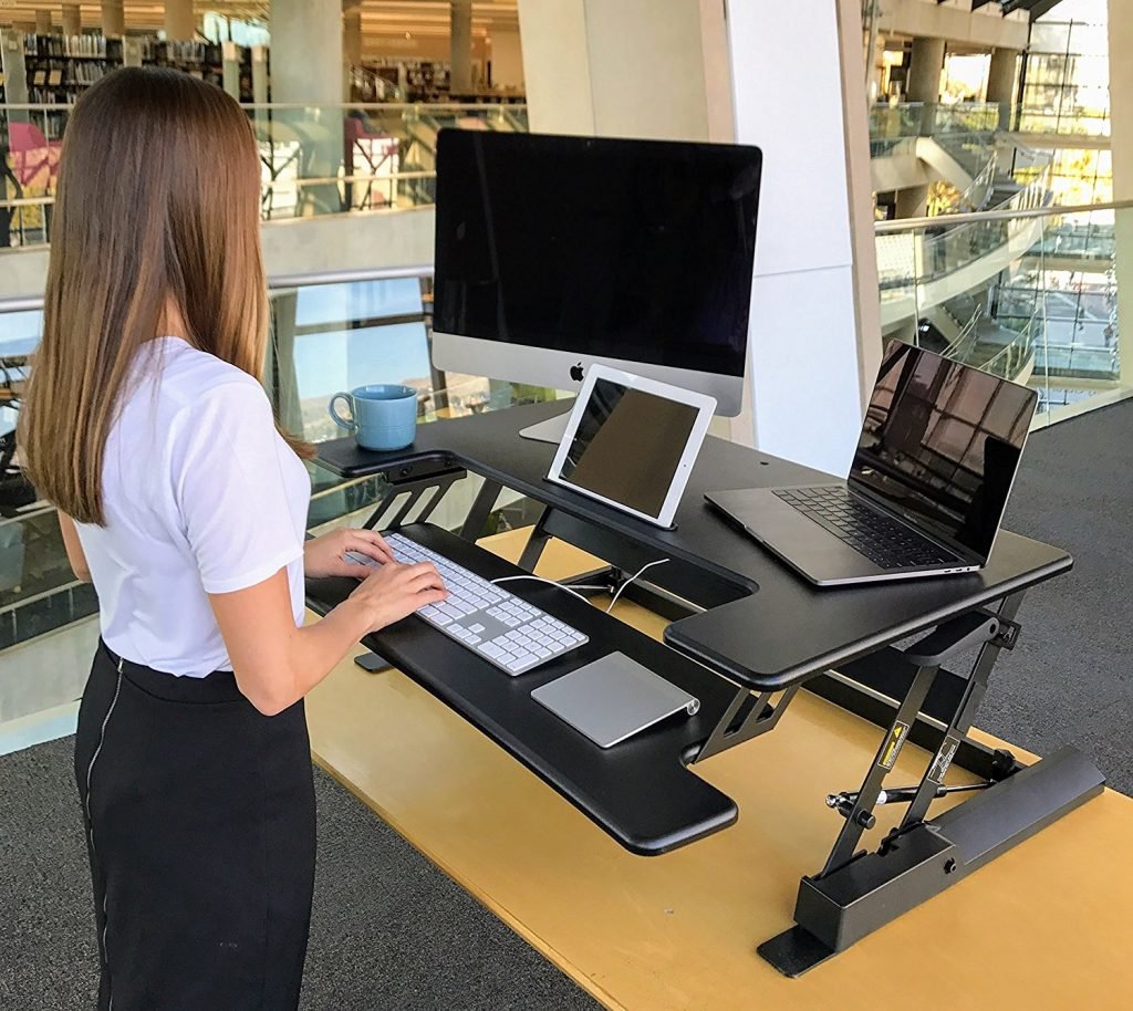 a woman with an iMac, laptop, and tablet on the deskdoc standing desk converter