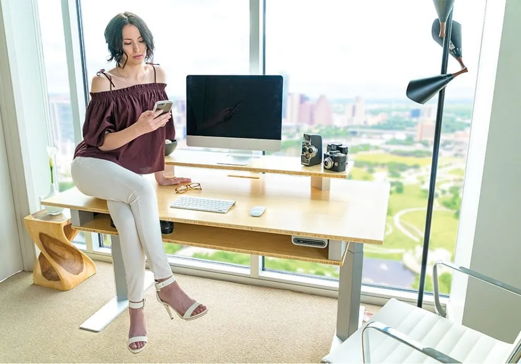 woman sitting on a xdesk terra stand up desk next to floor to ceiling windows