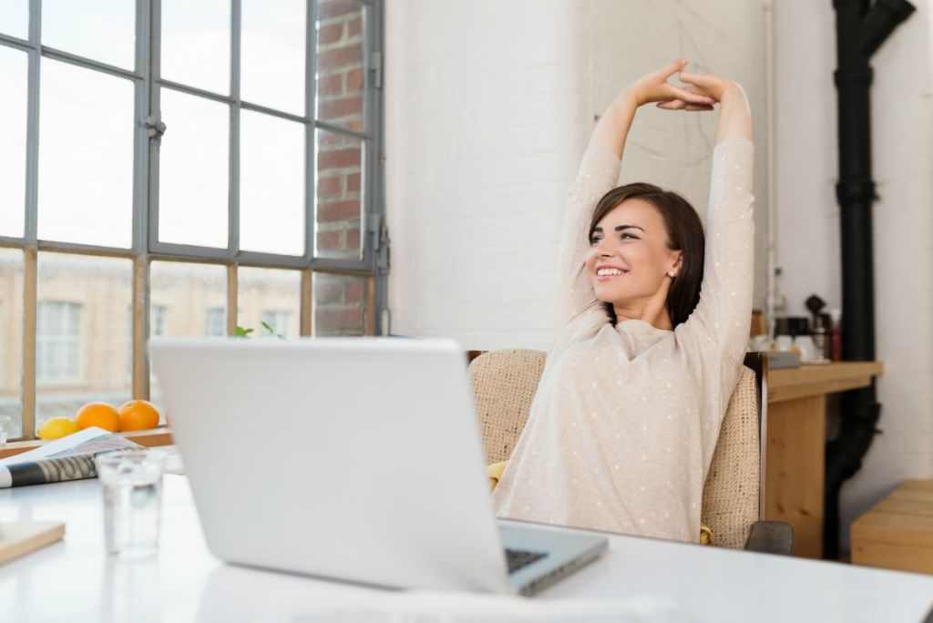 woman stretching at her desk with her laptop in front