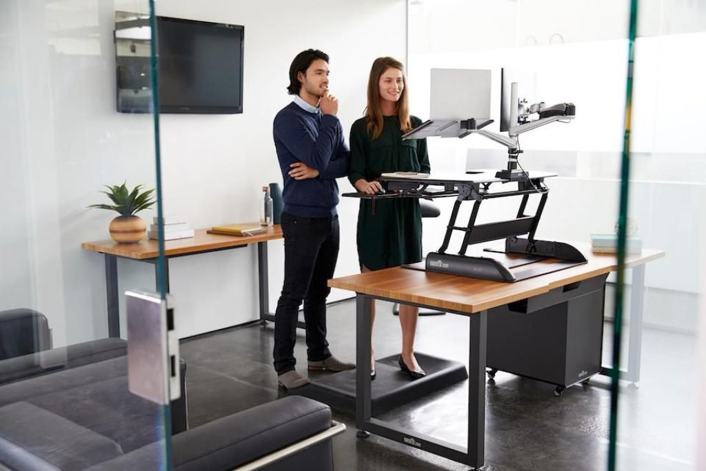 man and woman looking at a monitor screen using the varidesk stand up desk converter