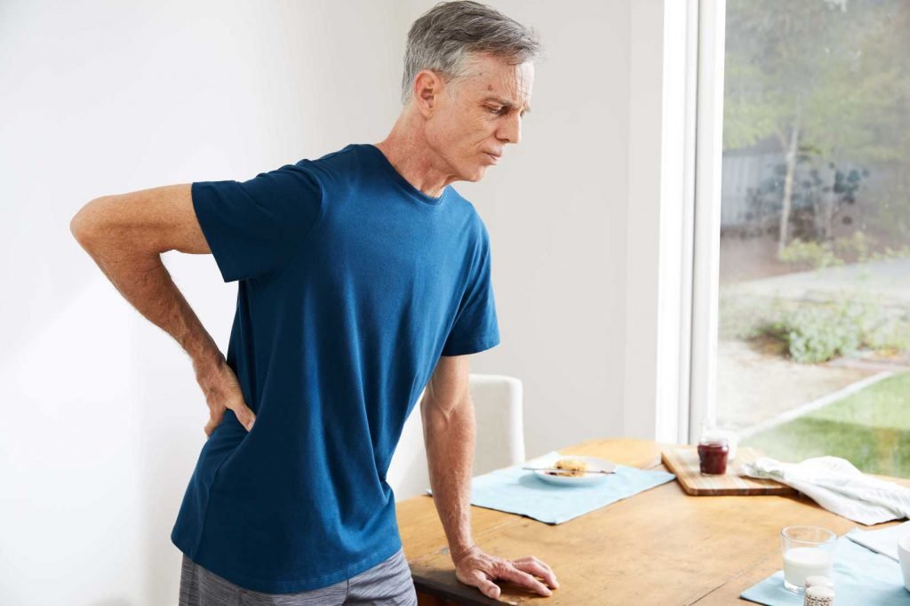 man holding his back next to his office desk. lower back pain when standing